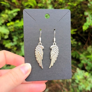 May include: Silver dangle earrings featuring a wing design. The wings are detailed and have a textured finish.
