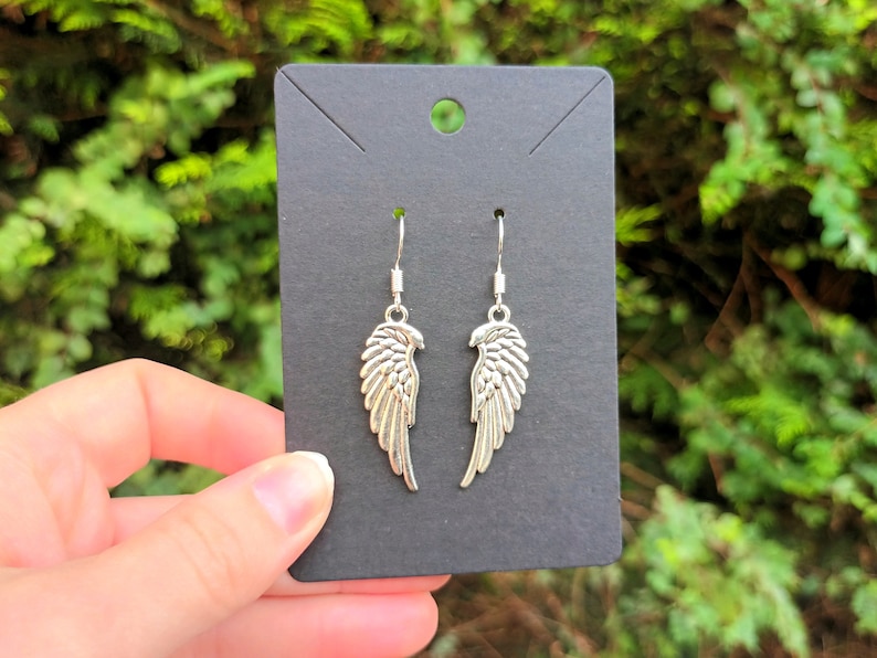 May include: Silver dangle earrings featuring a wing design. The wings are detailed and have a textured finish.