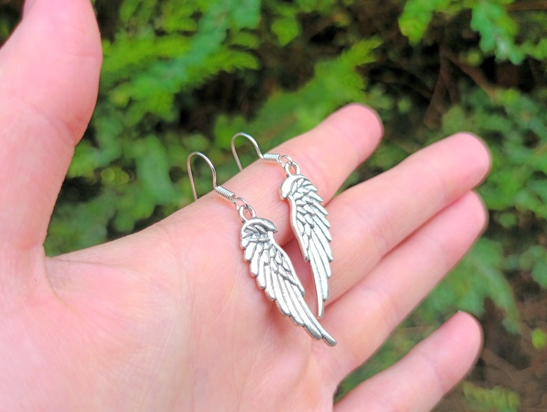 May include: A pair of silver dangle earrings featuring a wing design. The wings are detailed and have a slightly textured finish.