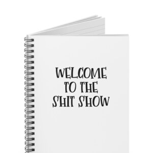 May include: White spiral bound notebook with the text "WELCOME TO THE S'HIT SHOW" printed in black.