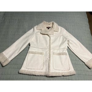 May include: Off-white jacket with a faux fur collar, cuffs, and trim. The jacket has two front pockets and a button-up closure. The jacket is made of a soft, suede-like material.