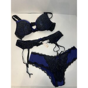 May include: A three-piece lingerie set in navy blue and black. The set includes a bra, garter belt, and thong. The bra and thong feature a dotted pattern and lace trim. The garter belt has adjustable straps and a small bow.