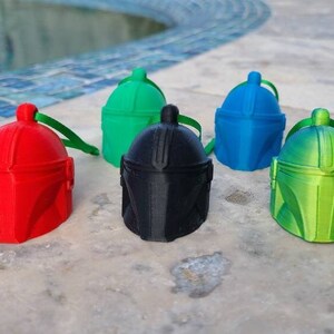 May include: Five Mandalorian helmet ornaments in different colors: red, black, green, blue, and green. The ornaments are made of plastic and have a shiny finish.
