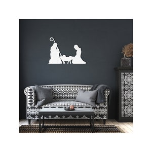May include: White silhouette of the nativity scene with Mary, Joseph, and baby Jesus in a manger. The silhouette is mounted on a dark grey wall above a black and white patterned sofa.