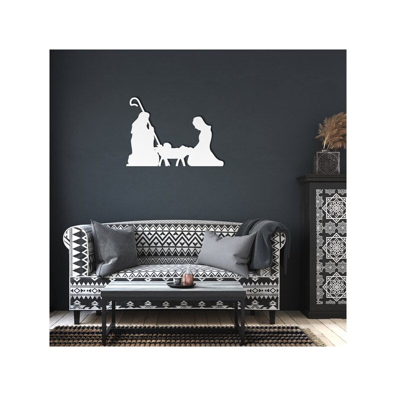 May include: White silhouette of the nativity scene with Mary, Joseph, and baby Jesus in a manger. The silhouette is mounted on a dark grey wall above a black and white patterned sofa.