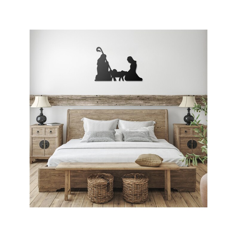 May include: A black metal silhouette of the nativity scene with Mary, Joseph, and the baby Jesus in a manger. The silhouette is mounted on a white wall above a wooden bed with a white duvet and pillows. Two wooden bedside tables with lamps are on either side of the bed.