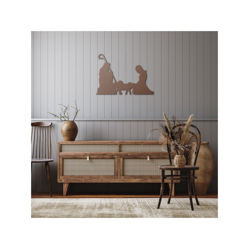 May include: A wooden wall decoration featuring a silhouette of the nativity scene. The decoration is brown and is mounted on a light grey wall. The decoration is displayed above a wooden dresser with a woven rattan front.