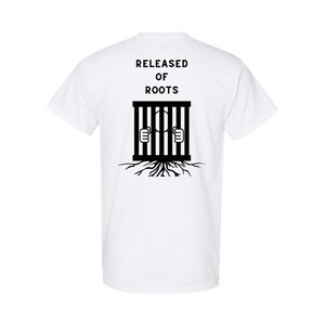 May include: White t-shirt with black text that reads "RELEASED OF ROOTS" and a black illustration of a person behind bars with roots growing from the bottom of the bars.