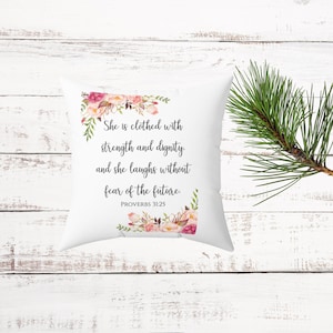May include: White throw pillow with pink floral design and the text "She is clothed with strength and dignity. and she laughs without fear of the future. PROVERBS 31:25"