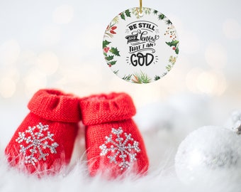 May include: A Christmas ornament with the text "BE STILL AND KNOW THAT I AM GOD" surrounded by a floral design. Two red knitted baby booties with silver snowflake designs are in the foreground.