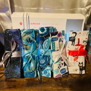May include: Six fabric pouches with different patterns and colors. The pouches are tied with ribbons and are arranged in a row on a wooden surface. The pouches are all different sizes and shapes. The pouches are made of fabric and have a variety of patterns, including stars, hearts, and cats.