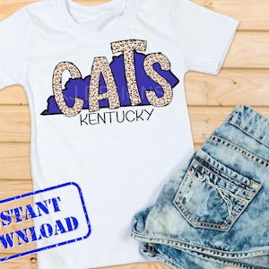 Peut inclure: T-shirt blanc avec un motif bleu et léopard de l'état du Kentucky avec le mot "CATS" au milieu et le mot "KENTUCKY" en dessous.