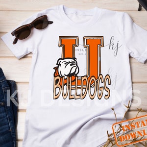 May include: White t-shirt with an orange and black bulldog graphic and the text "Bulldogs" in a vintage style font. The graphic includes the letter "U" in a large, bold font.