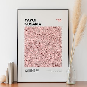 Może przedstawiać: Oprawiony wydruk z nazwą "YAYOI KUSAMA" w kolorze czarnym i "TOKYO 1998" w kolorze czerwonym. Grafika zawiera czerwono-biały wzór w kropki. Dodatkowy tekst w języku japońskim i francuskim jest również obecny.