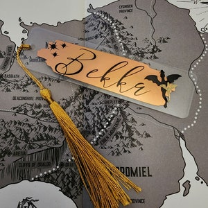 May include: A gold bookmark with the name "Bekka" written on it. The bookmark has a dragon design and a gold tassel.