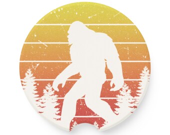 May include: A white silhouette of Bigfoot walking through a forest with a retro sunset background. The background is a gradient of orange, yellow, and red with a distressed look.