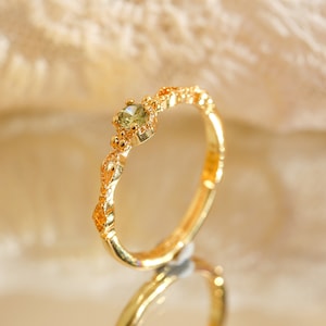 Può includere: Un anello d'oro con un design delicato e decorato e una piccola pietra preziosa verde chiaro al centro.