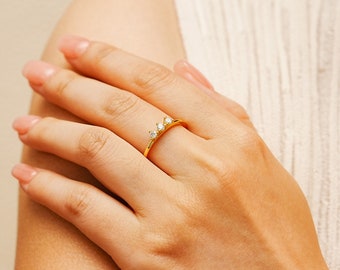 May include: A gold ring with three small clear stones set in a curved band.