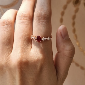 Può includere: Un anello in oro rosa con una pietra ovale rossa e pietre più piccole trasparenti su entrambi i lati.