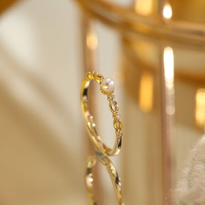 May include: A gold ring with a delicate design featuring a pearl and small clear stones.
