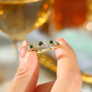 May include: A gold band ring with alternating green and clear round stones.
