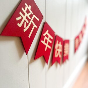 May include: Red and gold Chinese New Year banner with the characters "新年快乐" which translates to "Happy New Year".