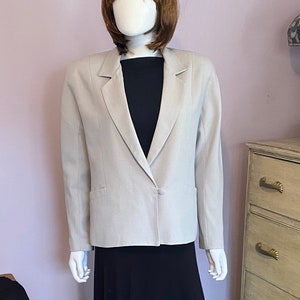 May include: A light gray blazer with a single button closure and a black skirt. The blazer has a notched collar and a pocket on the left side.
