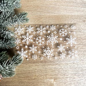 May include: A sheet of white snowflake stickers on a wood background. The snowflakes are various sizes and shapes.