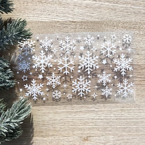 May include: A sheet of clear vinyl with white snowflake stickers. The snowflakes are of various sizes and designs.