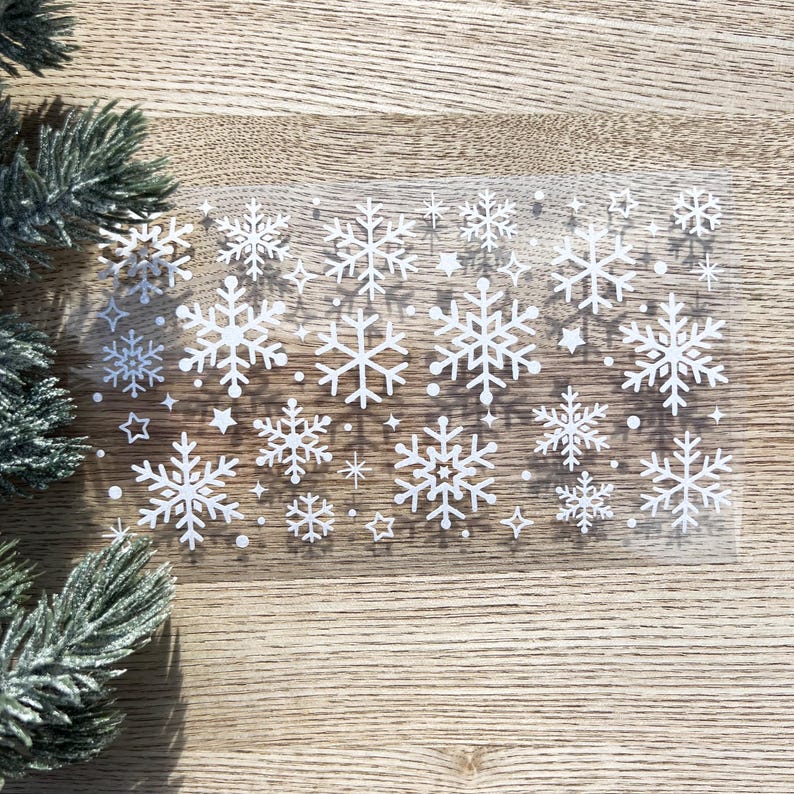 May include: A sheet of clear vinyl with white snowflake stickers. The snowflakes are of various sizes and designs.