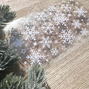 May include: A sheet of clear adhesive paper with white snowflake stickers. The snowflakes are various sizes and shapes.