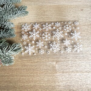 May include: A sheet of white snowflake stickers on a wood background. The snowflakes are various sizes and shapes.