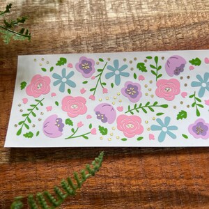 May include: A sheet of pink, purple and blue floral stickers with gold glitter accents. The stickers feature various flower shapes and sizes, including roses, daisies and smaller flowers.