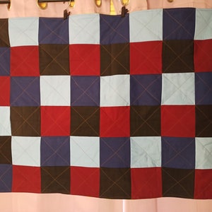 May include: A quilted throw blanket with a checkered pattern in red, blue, black, and light blue.