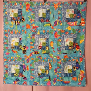 May include: A blue and green patchwork quilt with a sea life theme. The quilt features various colorful fish, starfish, and seaweed patterns.