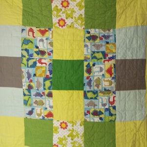 May include: A patchwork quilt with a green, yellow, and blue color scheme. The quilt features a variety of patterns, including dinosaurs, frogs, and flowers.
