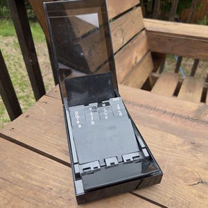 Peut inclure: Un organiseur de bureau pour fiches d'adresses en plastique noir avec un couvercle transparent articulé. L'intérieur présente une série d'intercalaires alphabétiques noirs marqués de lettres blanches, dont a, b, c, d, u, v, w et xyz.