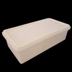 Puede incluir: Un recipiente rectangular de plástico blanquecino con tapa a juego. El recipiente tiene un diseño ligeramente curvado y está sobre un fondo negro. La tapa encaja perfectamente encima.