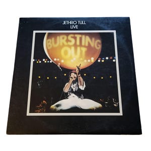 May include: A vintage vinyl record album cover for Jethro Tull's live album, "Bursting Out." The cover features a stage performance scene with a large, illuminated orange sphere and the band's name at the top. The album is in a black sleeve.