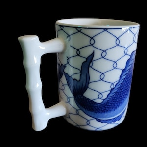 Puede incluir: Taza de cerámica blanca con asa de bambú. La taza presenta un diseño de pez azul y un patrón de celosía azul sobre fondo blanco. Adecuada para bebidas frías o calientes.
