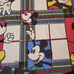 Peut inclure: Un tissu &agrave; motif &eacute;cossais avec Mickey Mouse dans diverses poses. Les carr&eacute;s ont un fond blanc avec Mickey Mouse dans des carr&eacute;s rouges et bleus. Le motif &eacute;cossais a des rayures rouges, vertes, bleues et jaunes.