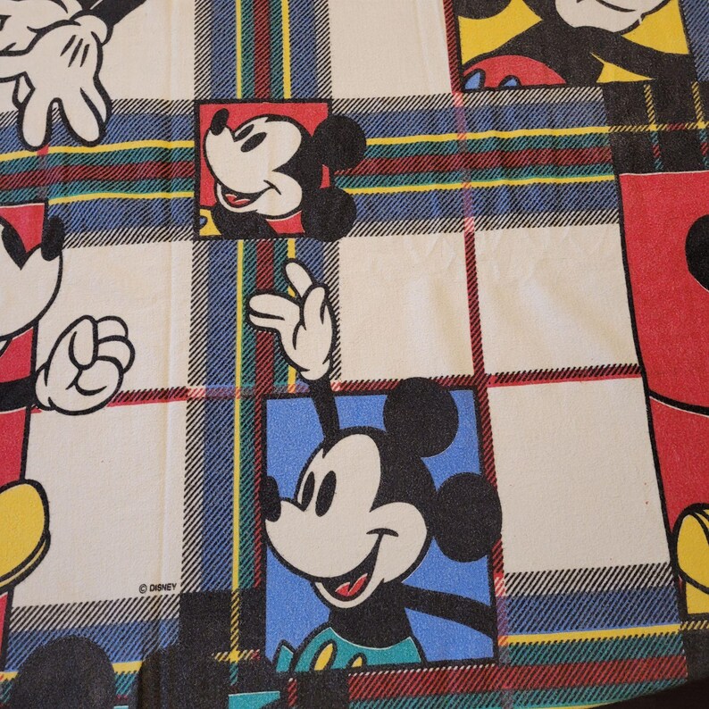 Peut inclure: Un tissu &agrave; motif &eacute;cossais avec Mickey Mouse dans diverses poses. Les carr&eacute;s ont un fond blanc avec Mickey Mouse dans des carr&eacute;s rouges et bleus. Le motif &eacute;cossais a des rayures rouges, vertes, bleues et jaunes.