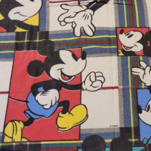 Peut inclure: Tissu avec un motif r&eacute;p&eacute;titif de Mickey Mouse dans diverses poses. Le fond est un motif &agrave; carreaux en blanc, bleu, rouge, jaune et vert. Mickey porte un short bleu et des chaussures jaunes.