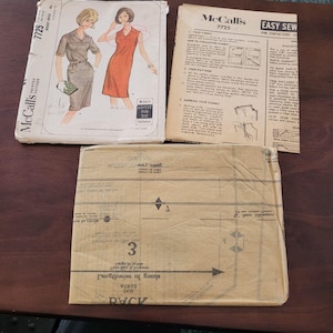 May include: A vintage sewing pattern for a dress, McCall's 7725, with instructions for easy sewing. The pattern includes a front and back piece, and a separate instruction sheet. The pattern is printed on brown paper with black text.