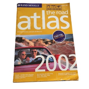 Puede incluir: Un atlas de carreteras Rand McNally de 2002 para Estados Unidos, Canadá y México. La portada es amarilla con el título "the road atlas" en letras blancas grandes. Se presenta una foto de una pareja en un descapotable rojo. Incluye un directorio de Wal-Mart.
