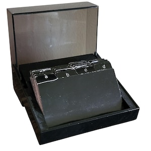 May include: A black index card box with a clear lid, open to reveal a set of alphabetized index cards. The cards are black with white lettering, and the box is made of a glossy material.