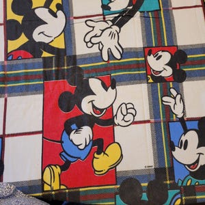 Peut inclure: Un tissu color&eacute; avec plusieurs images de Mickey Mouse dans diff&eacute;rentes poses. Les images sont plac&eacute;es sur un fond &agrave; carreaux avec des rayures rouges, bleues, jaunes et vertes. Mickey porte un short bleu et des chaussures jaunes.