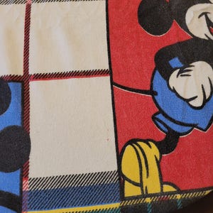 Peut inclure: Un tissu color&eacute; avec un motif de personnage de dessin anim&eacute; Mickey Mouse. Le tissu a un fond rouge avec Mickey Mouse en noir, bleu et jaune. Une section du tissu a un fond blanc avec un motif &agrave; carreaux noir, rouge et bleu.