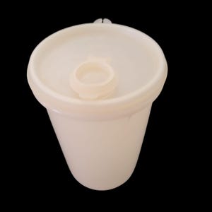 May include: A white plastic container with a lid and a small, circular insert. The container has a slightly tapered shape and a smooth surface. The lid has a small handle for easy opening.