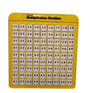 Puede incluir: Una máquina de multiplicar Lakeshore amarilla con una cuadrícula de botones cuadrados blancos. Cada botón muestra una ecuación de multiplicación que va de 1x1 a 9x9. La parte superior del marco de plástico presenta el texto Multiplication Machine en negro.